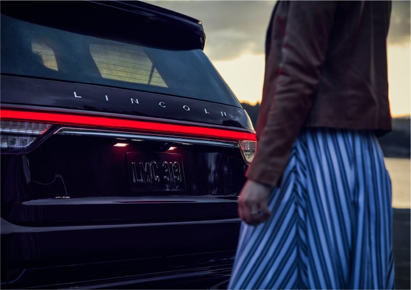 A person is shown near the rear of a 2023 Lincoln Aviator® SUV as the Lincoln Embrace illuminates the rear lights | Courtesy Lincoln in Altoona PA