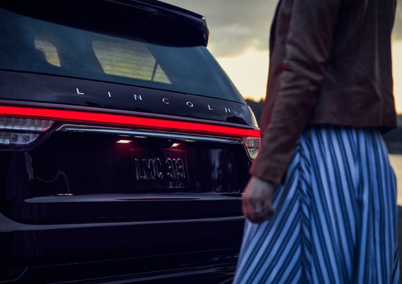 A person is shown near the rear of a 2024 Lincoln Aviator® SUV as the Lincoln Embrace illuminates the rear lights | Courtesy Lincoln in Altoona PA