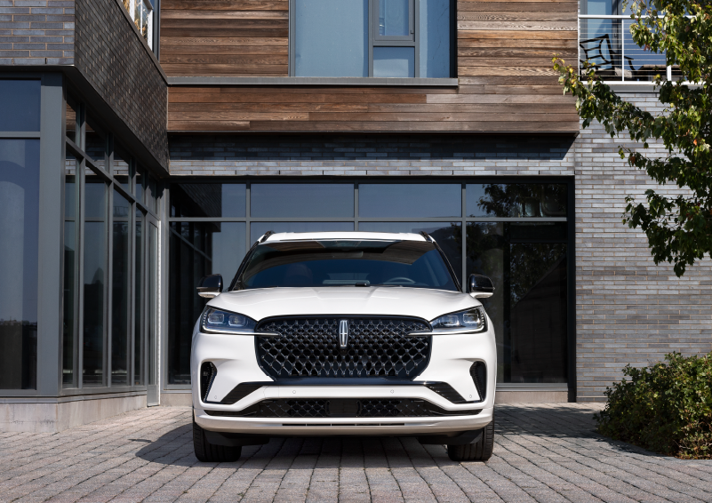 A white 2025 Lincoln Aviator® SUV is shown parked outside a modern building with gray brick and wood accents. | Courtesy Lincoln in Altoona PA