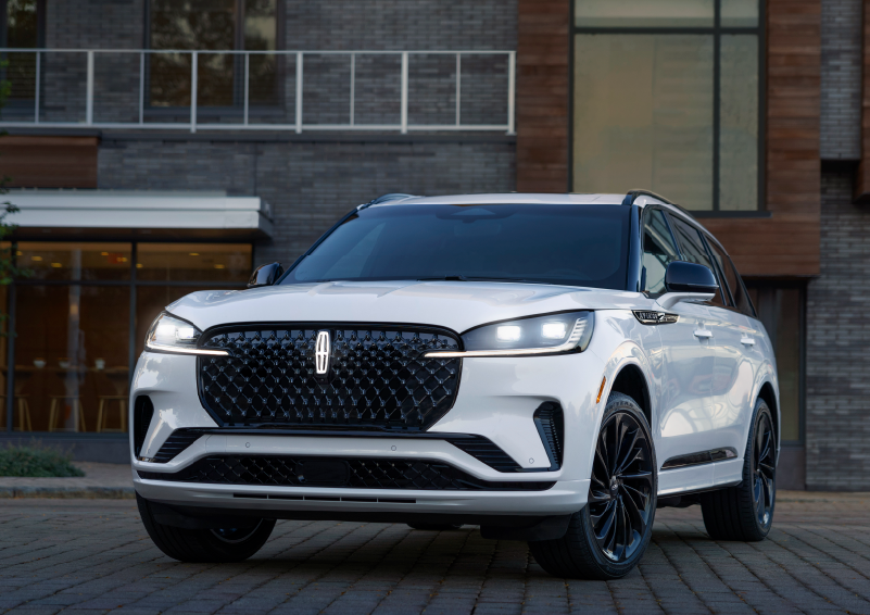 A white 2025 Lincoln Aviator® SUV is shown parked outside a modern building with gray brick and wood accents. | Courtesy Lincoln in Altoona PA
