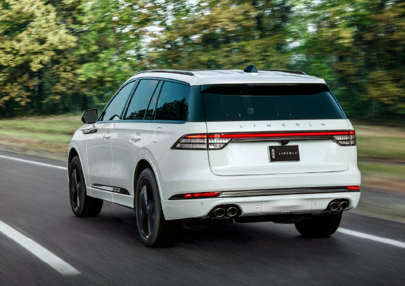 A white 2026 Lincoln Aviator® SUV is being driven away down a road lined with colorful trees. | Courtesy Lincoln in Altoona PA