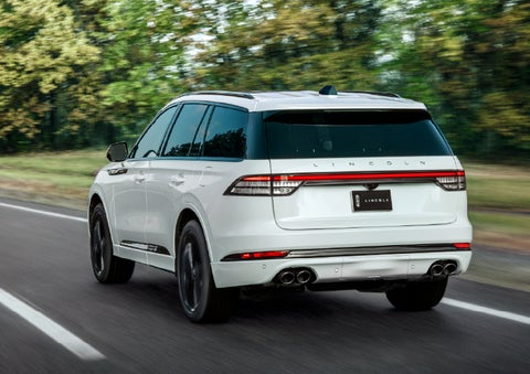 A white 2026 Lincoln Aviator® SUV is being driven away down a road lined with colorful trees. | Courtesy Lincoln in Altoona PA